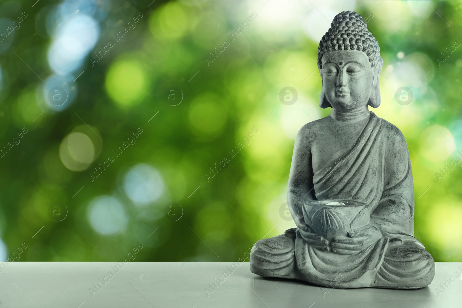 Image of Stone Buddha sculpture on table outdoors. Space for text