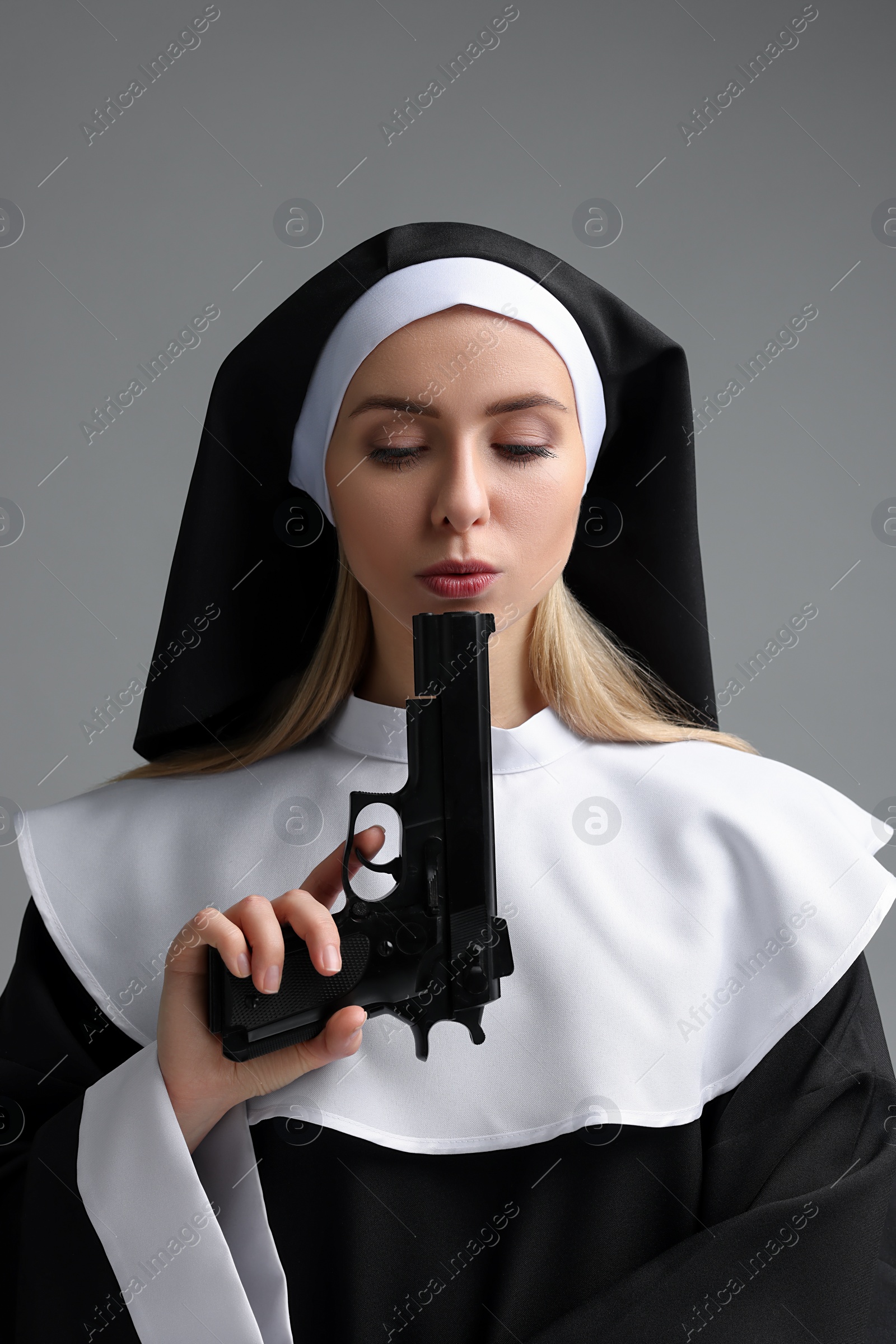 Photo of Woman in nun habit holding handgun on grey background