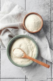 Photo of Bowls and spoon of agar-agar powder on tiled table, flat lay