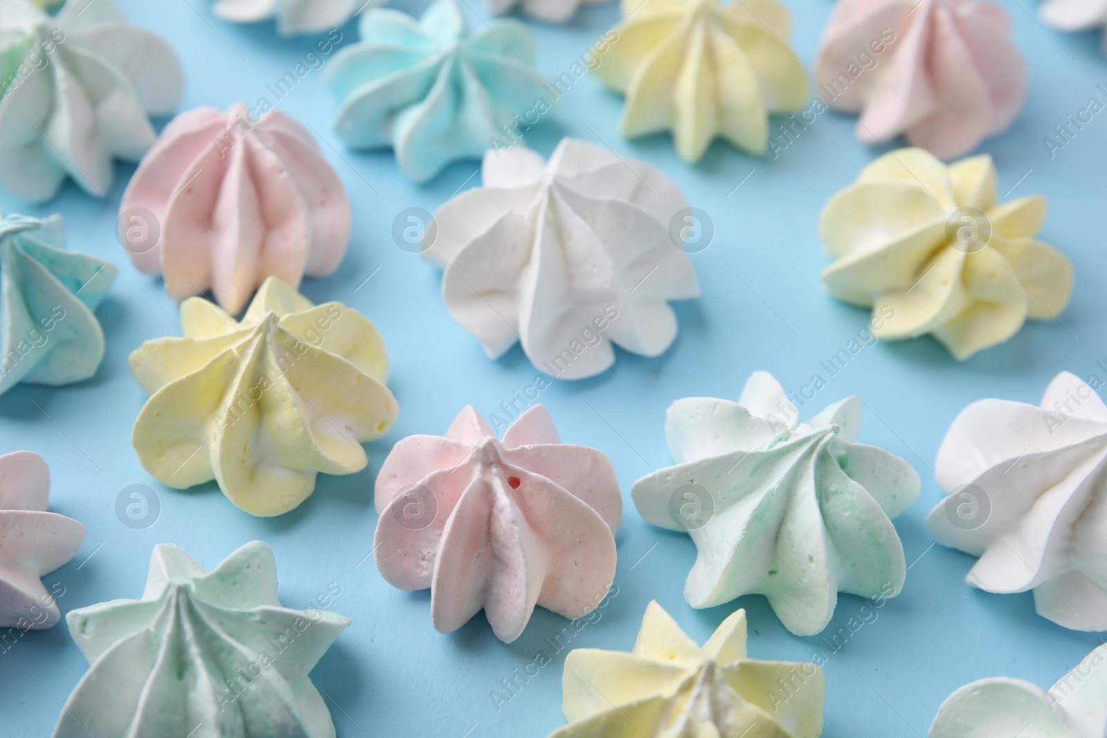 Photo of Tasty meringue cookies on light blue background, closeup