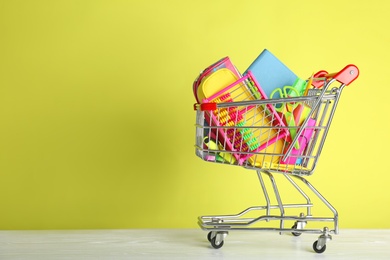 Photo of Small shopping cart with different school stationery on color background