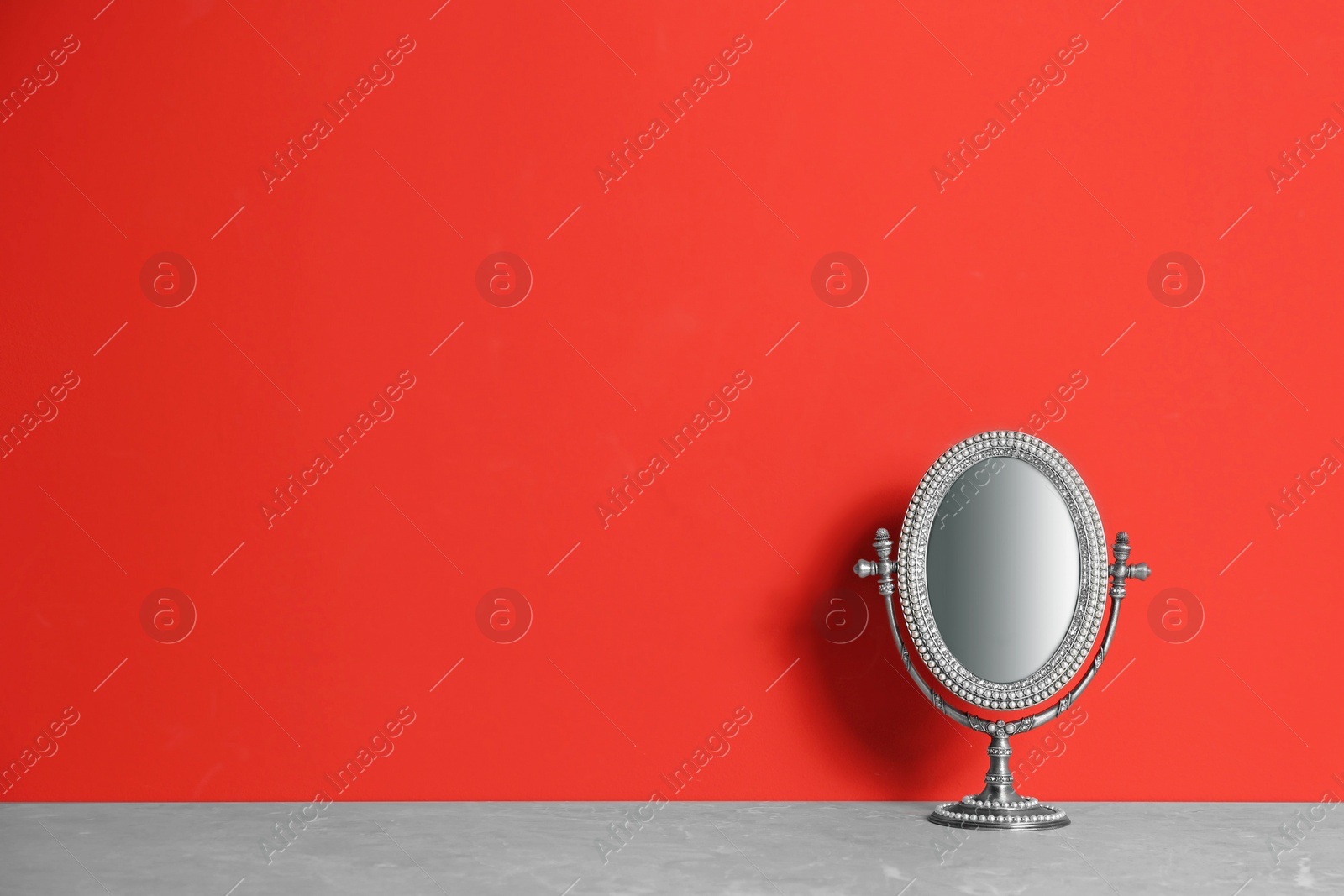 Photo of Small mirror on grey marble table near red wall. Space for text
