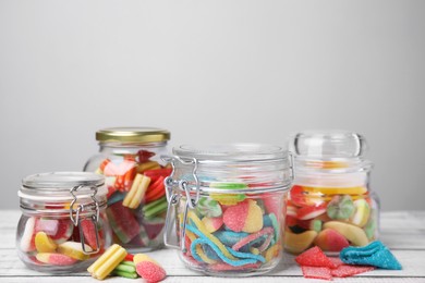 Tasty jelly candies in different jars on white wooden table, space for text