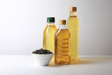 Photo of Bottles of different cooking oils and sunflower seeds on white background, space for text