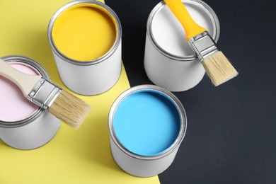 Photo of Cans of colorful paints and brushes on color background, above view