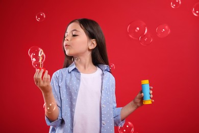 Photo of Little girl blowing soap bubbles on red background