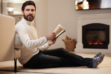 Handsome man reading book near fireplace in room