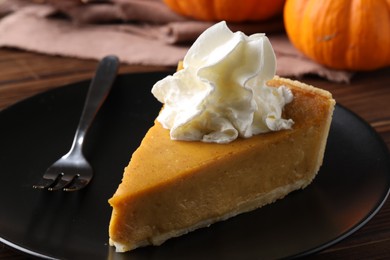 Piece of delicious pumpkin pie with whipped cream and fork on table, closeup