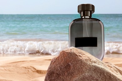 Bottle of aquatic perfume on rock near ocean. Fresh sea breeze scent