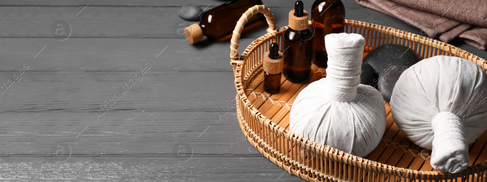 Image of Herbal massage bags, essential oils and spa stones on grey wooden table, space for text. Banner design