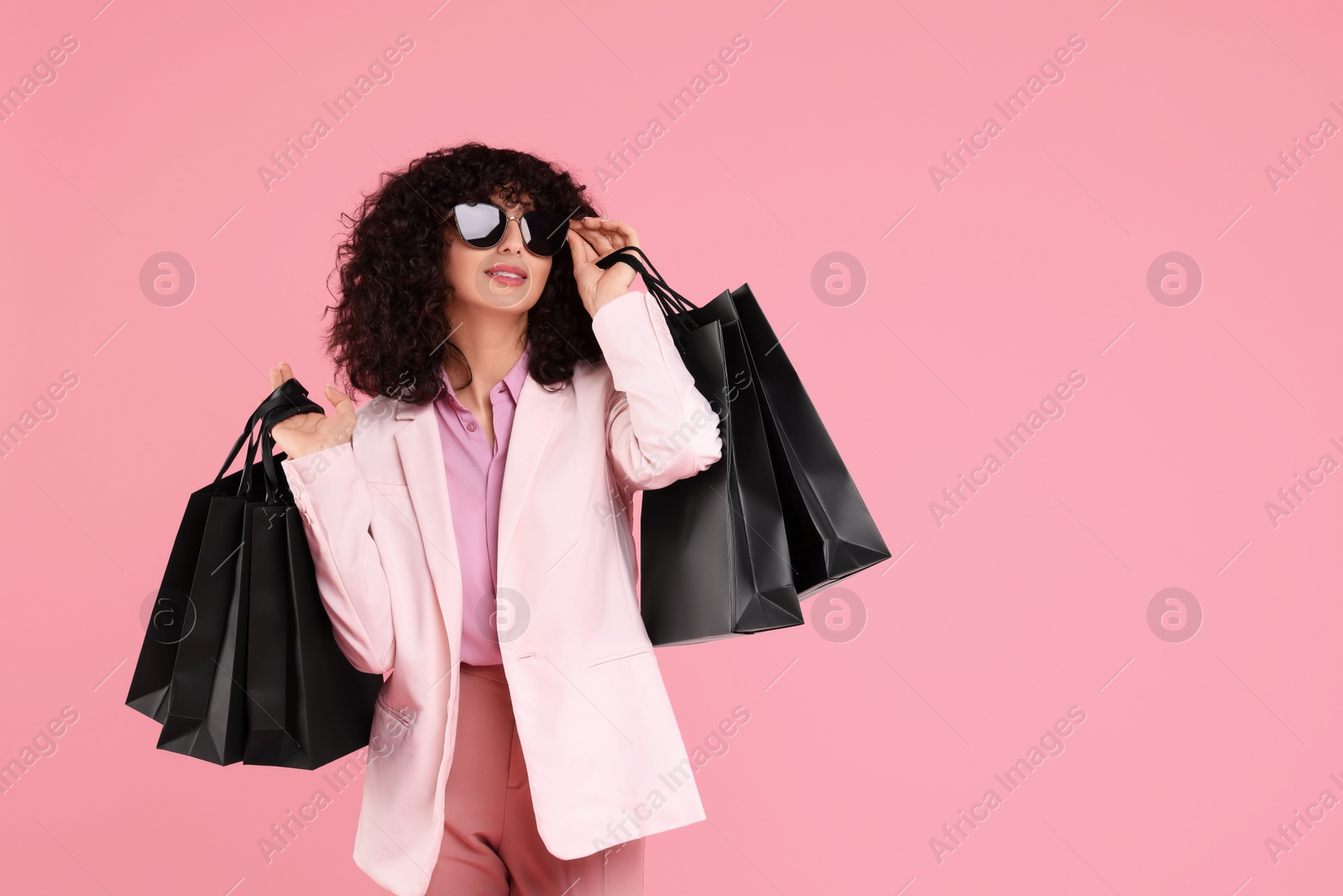 Photo of Happy young woman with shopping bags and stylish sunglasses on pink background. Space for text