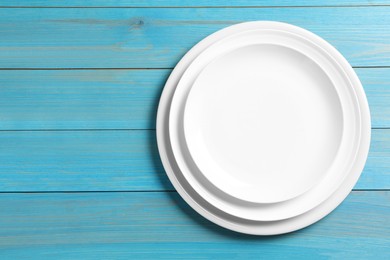 Photo of Stack of empty ceramic plates on turquoise wooden table, top view. Space for text