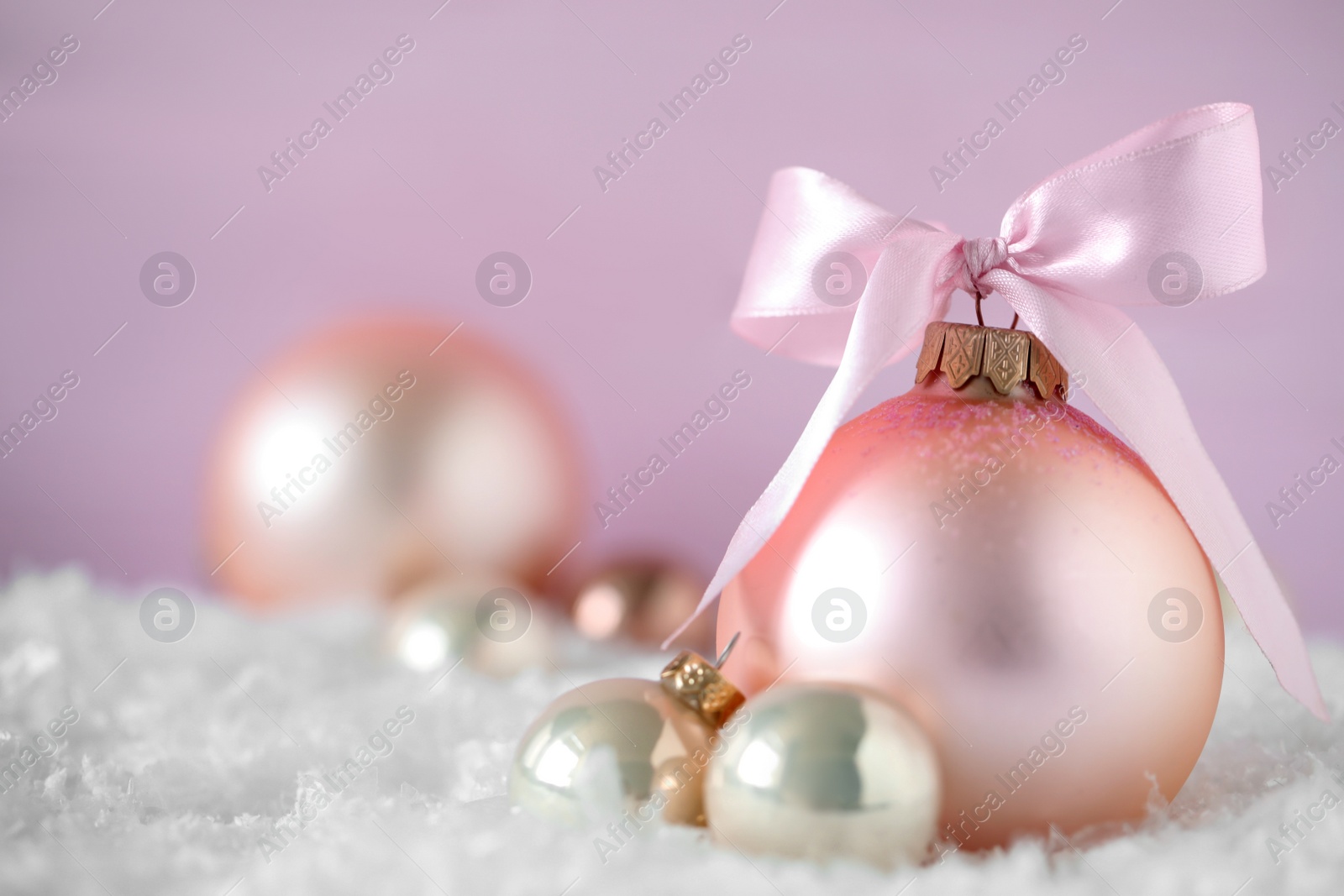 Photo of Beautiful Christmas balls on snow against pink background. Space for text