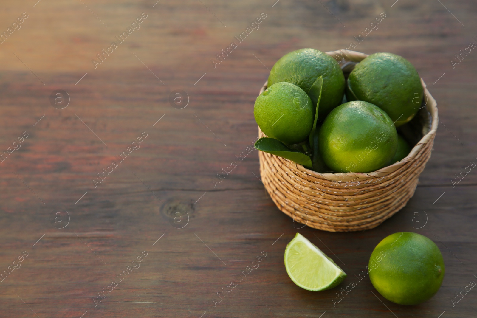 Photo of Fresh ripe limes and wicker basket on wooden table. Space for text