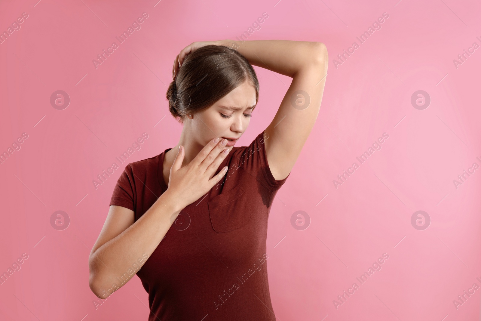 Photo of Young woman with sweat stain on her clothes against pink background. Using deodorant