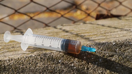 Photo of Syringe with hard drugs on stone surface outdoors, closeup