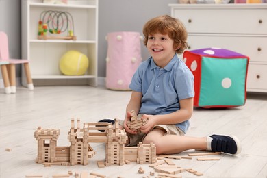 Little boy playing with wooden construction set on floor in room. Child's toy