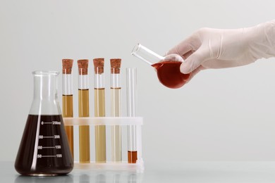 Photo of Scientist pouring brown liquid from round bottom flask into test tube on light background, closeup