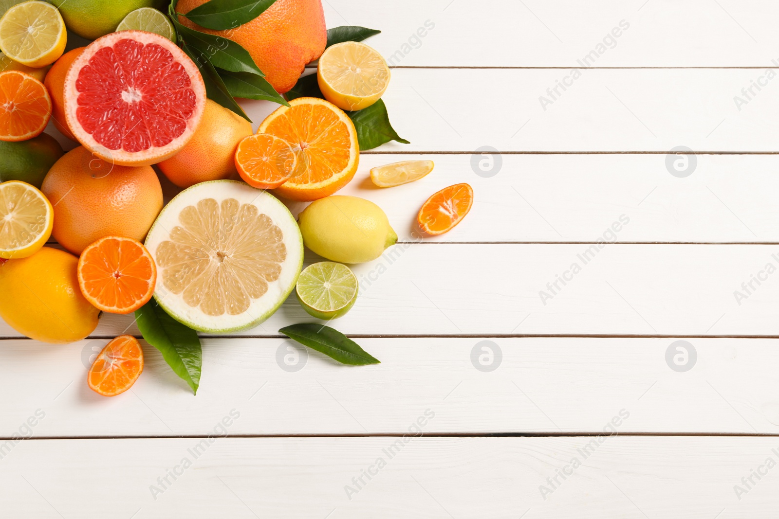 Photo of Different citrus fruits with fresh leaves on white wooden table, flat lay. Space for text