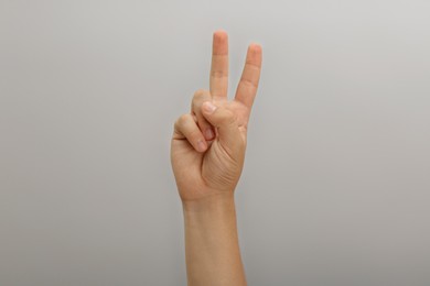 Photo of Teenage boy showing two fingers on light background, closeup