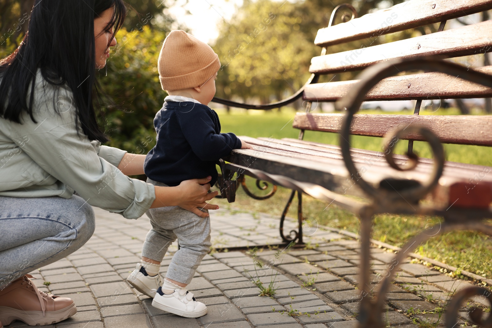 Photo of Mother supporting her baby while he learning to walk outdoors