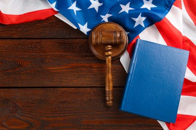 Judge's gavel, book and American flag on wooden table, flat lay. Space for text