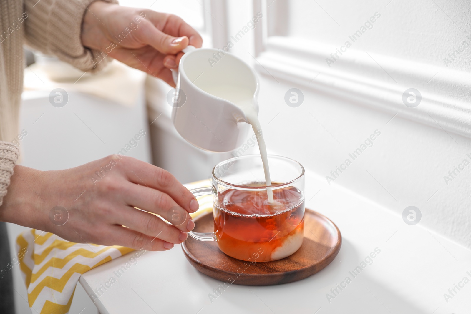 Photo of Woman pouring milk into cup of tea at white table, closeup