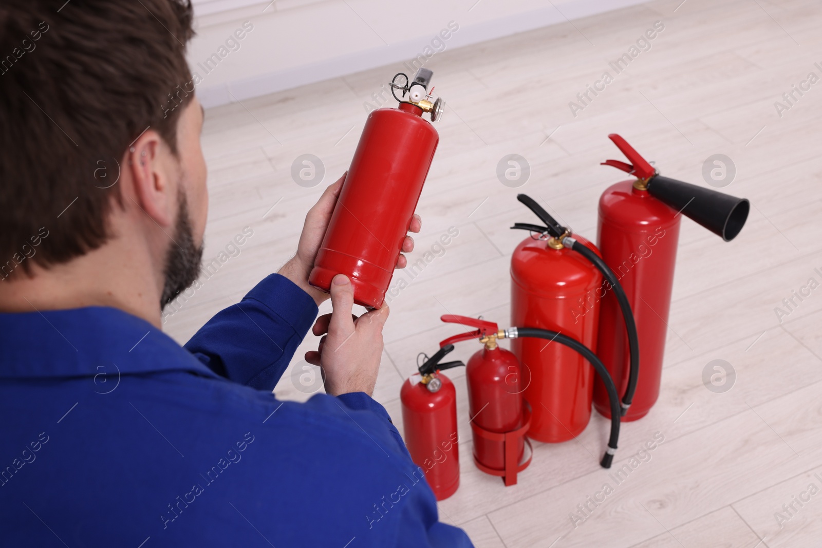 Photo of Man checking quality of fire extinguishers indoors, closeup