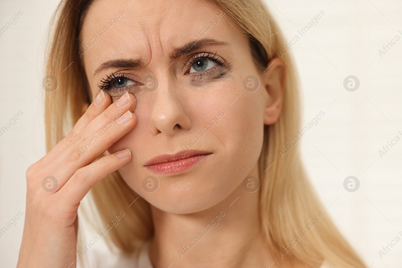 Photo of Sad woman with smeared mascara crying indoors, closeup