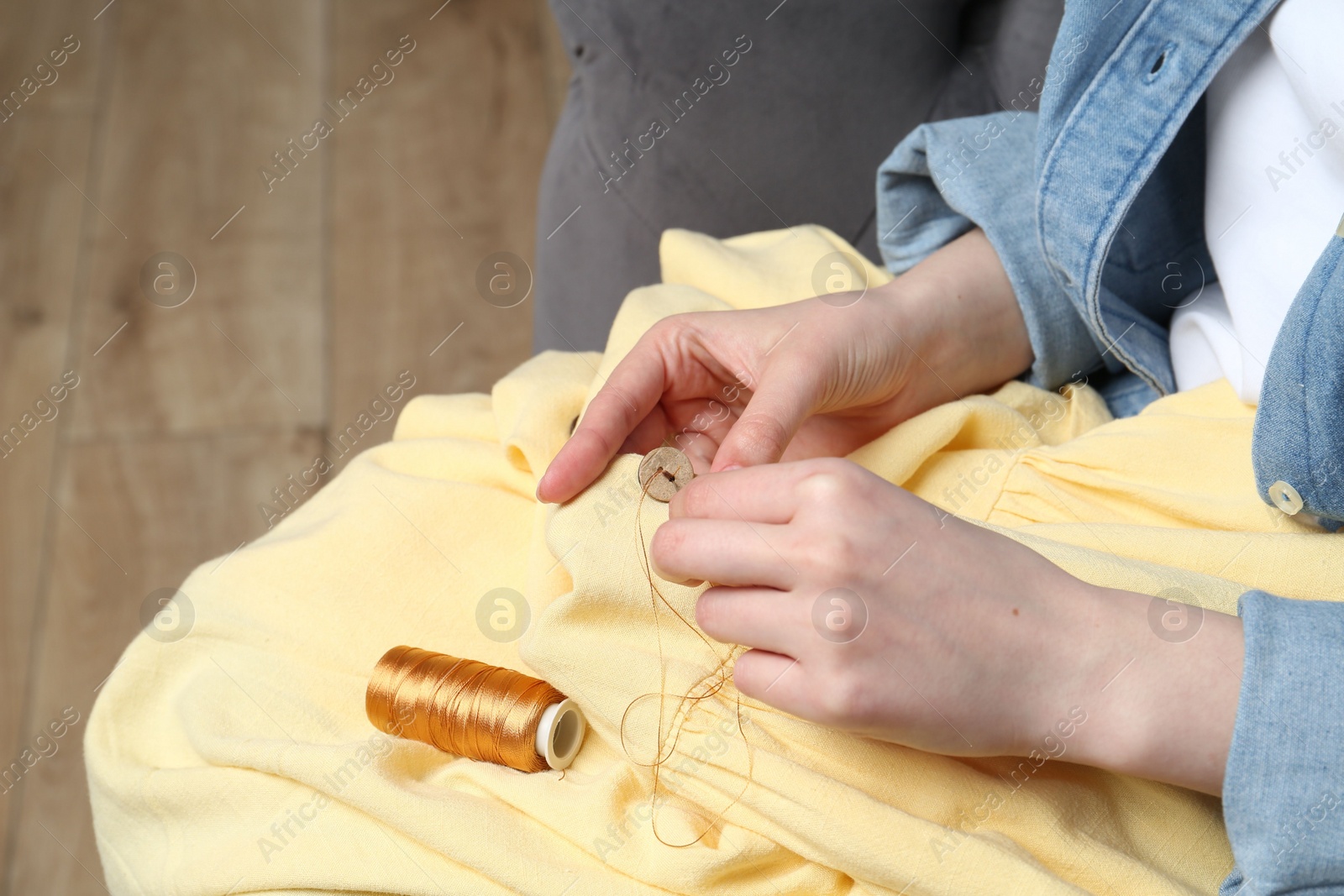 Photo of Woman sewing button with needle and thread onto shirt at home, closeup