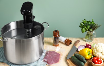 Photo of Meat in vacuum packing and other ingredients near pot with sous vide cooker on wooden table. Thermal immersion circulator