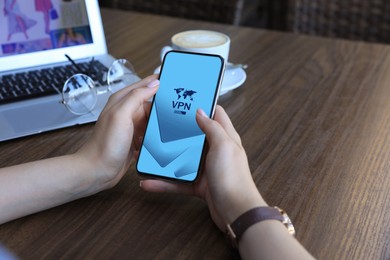 Image of Woman using smartphone with switched on VPN at wooden table, closeup