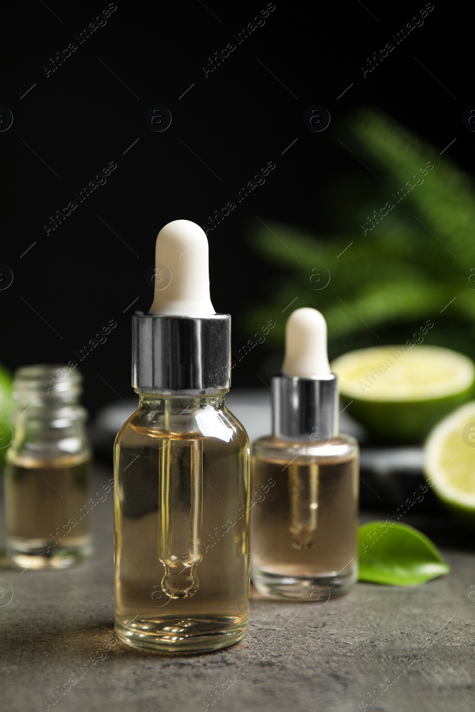 Photo of Lime essential oil and cut citrus fruits on grey table