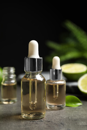 Lime essential oil and cut citrus fruits on grey table