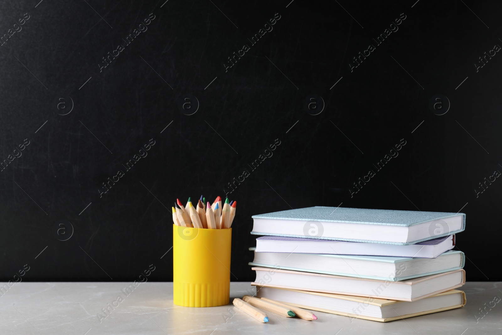 Photo of Stack of hardcover books and color pencils on table against black background. Space for text