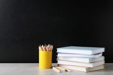 Photo of Stack of hardcover books and color pencils on table against black background. Space for text