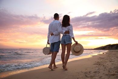 Lovely couple walking on beach at sunset, back view