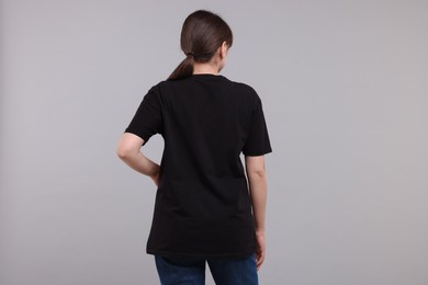 Photo of Woman in stylish black t-shirt light grey on background, back view