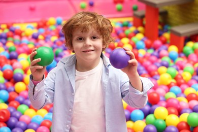 Photo of Happy little boy holding colorful balls in ball pit