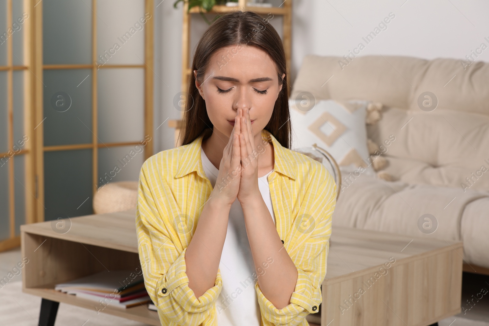 Photo of Woman with clasped hands praying at home