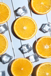 Slices of juicy orange and ice cubes on light blue background, flat lay