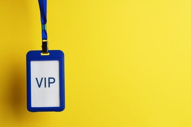 Photo of Blue plastic vip badge hanging on yellow background, space for text