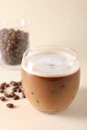 Refreshing iced coffee with milk in glass and beans on beige background