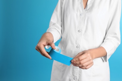 Photo of Female doctor holding elastic therapeutic tape on color background, closeup view with space for text. Medical object