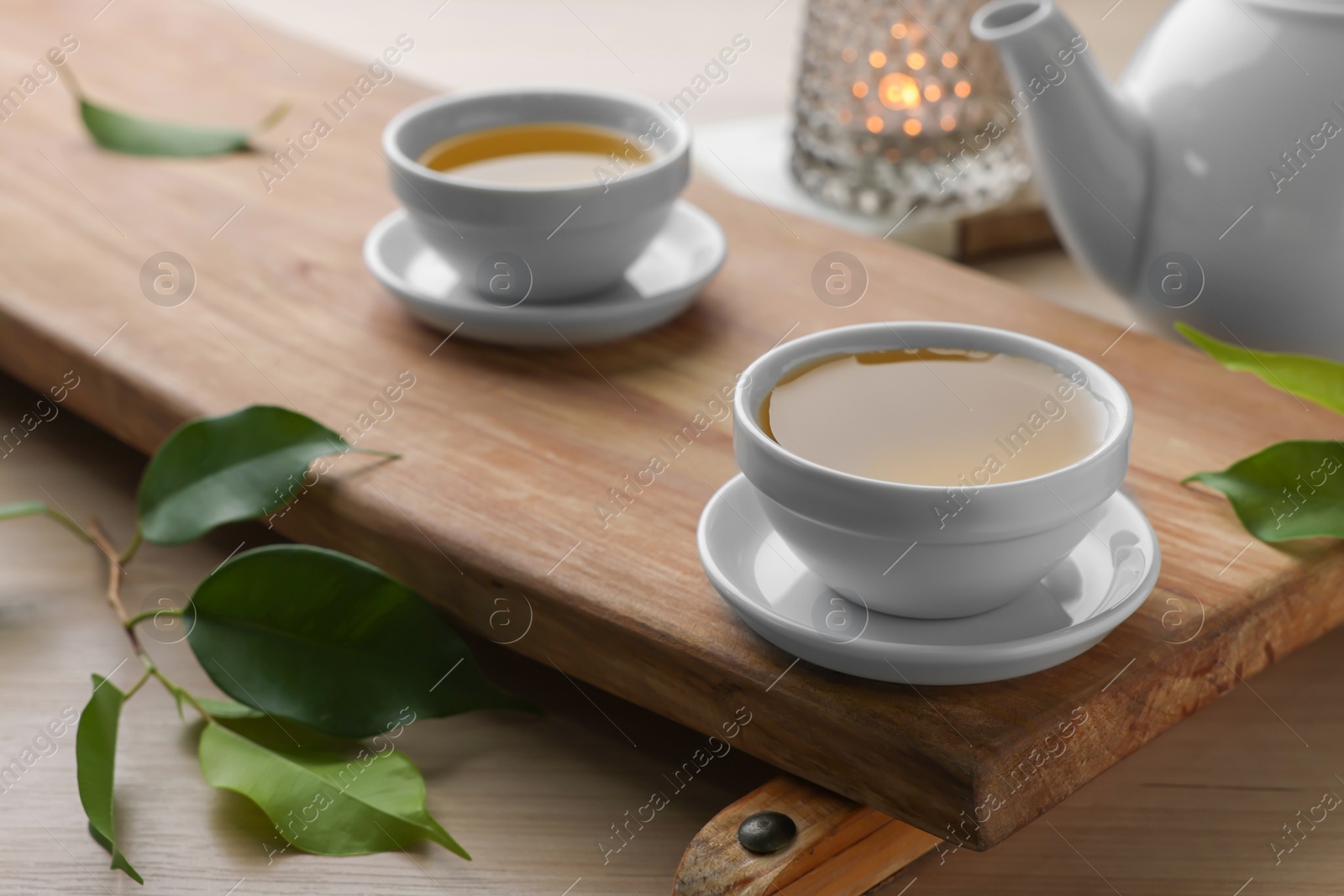 Photo of Tray with white cups of green tea, leaves and teapot on wooden table, closeup