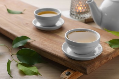 Tray with white cups of green tea, leaves and teapot on wooden table, closeup