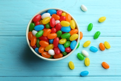 Bowl with colorful jelly beans on light blue wooden background, flat lay