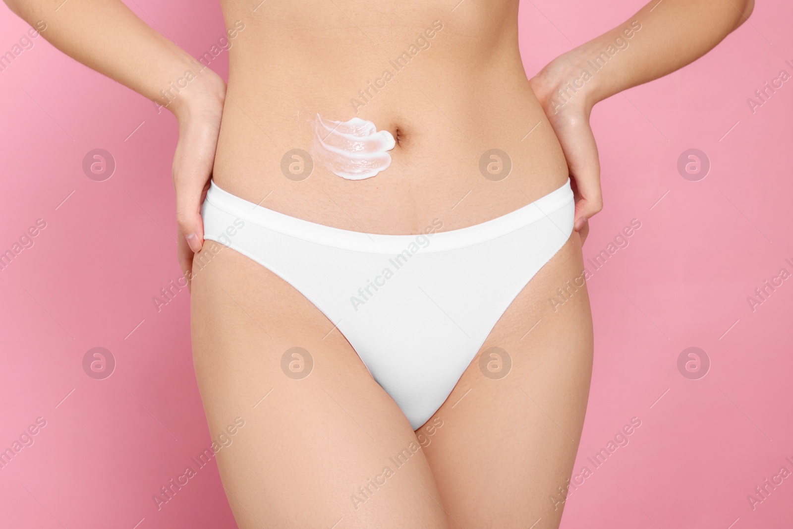 Photo of Woman with smear of body cream on belly against pink background, closeup