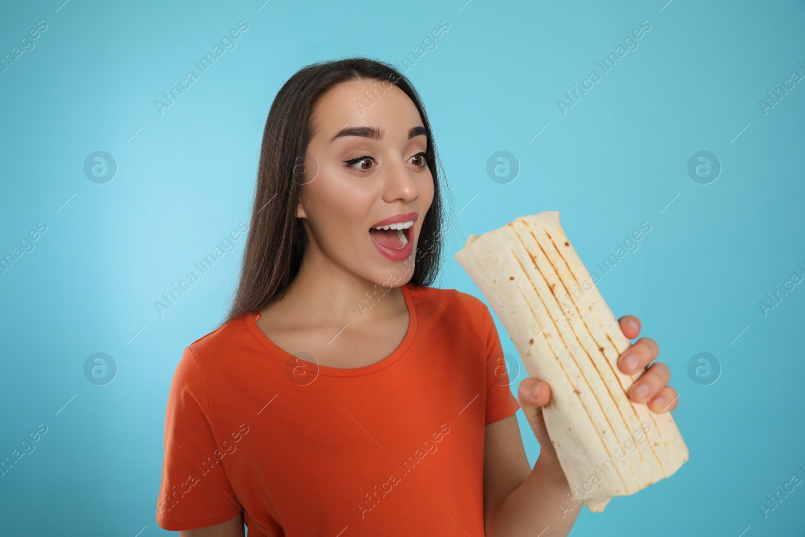 Photo of Young woman eating tasty shawarma on turquoise background