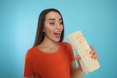 Young woman eating tasty shawarma on turquoise background